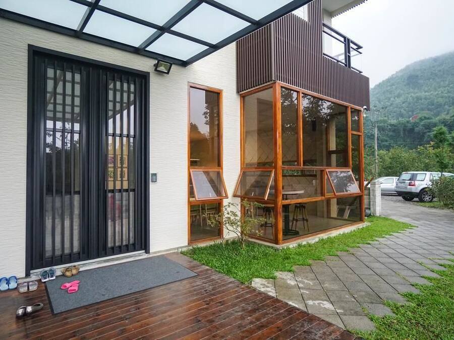 Una casa moderna con un amplio ventanal, una terraza de madera y vistas a un paisaje verde.