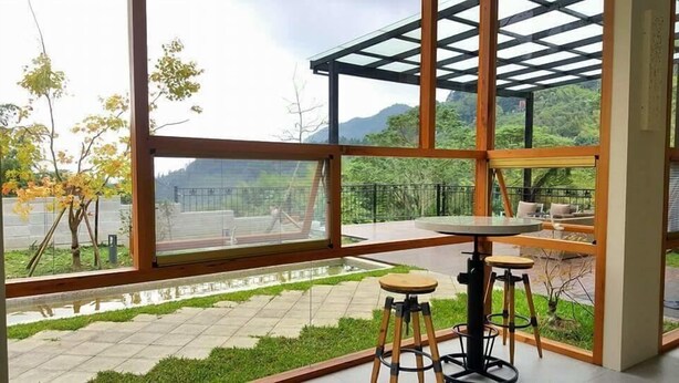 Ein modernes Interieur mit großen Fenstern, einem Glastisch und Blick auf einen Park und Berge.