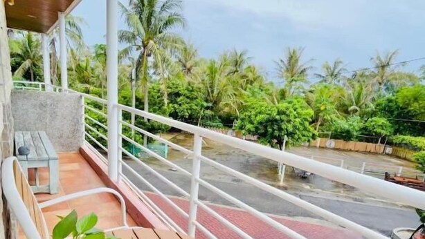 A balcony with a wooden table and chairs, a potted plant, and a view of a waterway with palm trees. - Li Ting B&B (Hengchun)