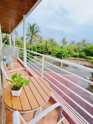 A balcony with a wooden table and chairs, a potted plant, and a view of a waterway with palm trees. - Li Ting B&B (Hengchun)