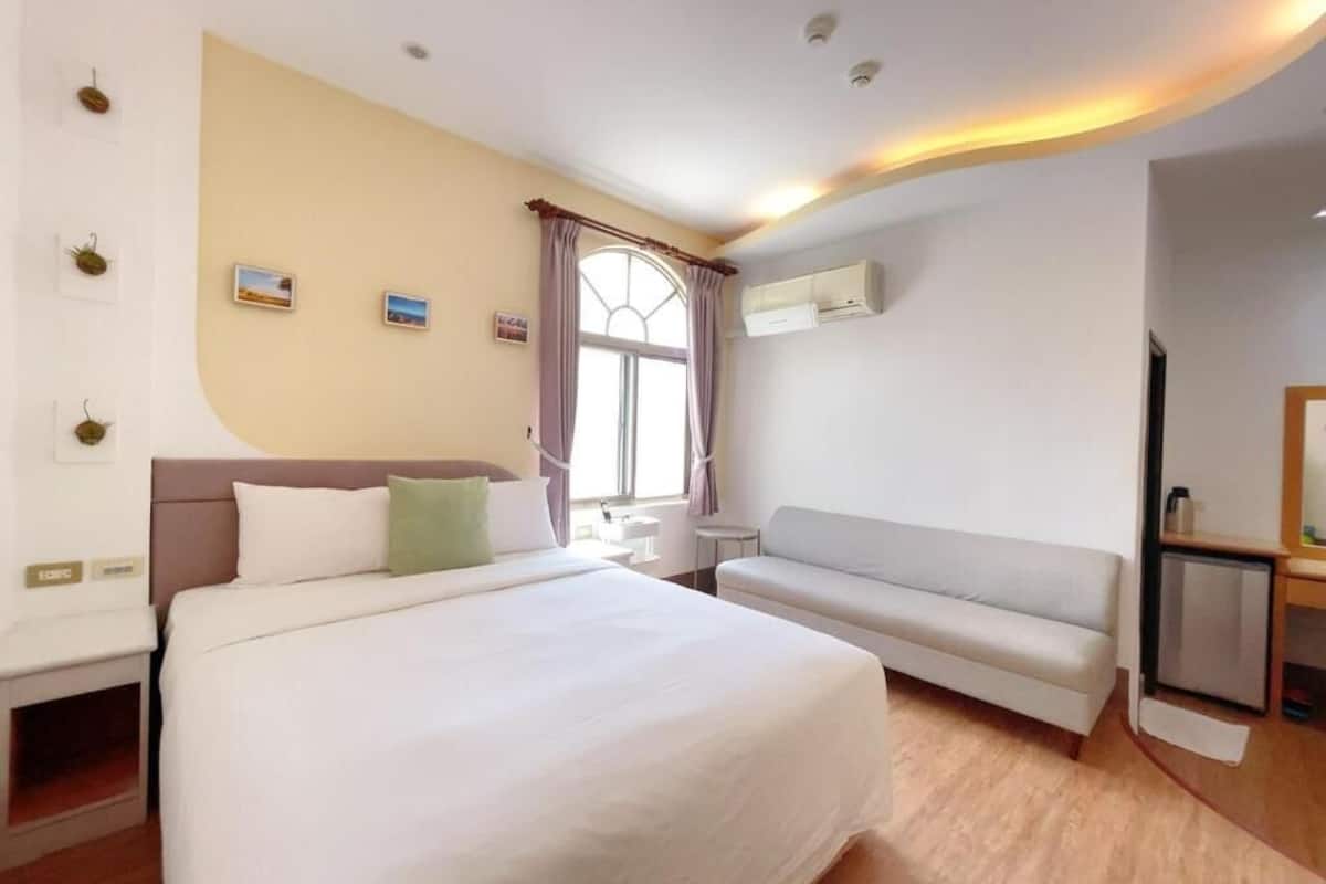 Habitación de hotel con una cama grande, un sofá, un equipo de aire acondicionado y una pequeña mesa.