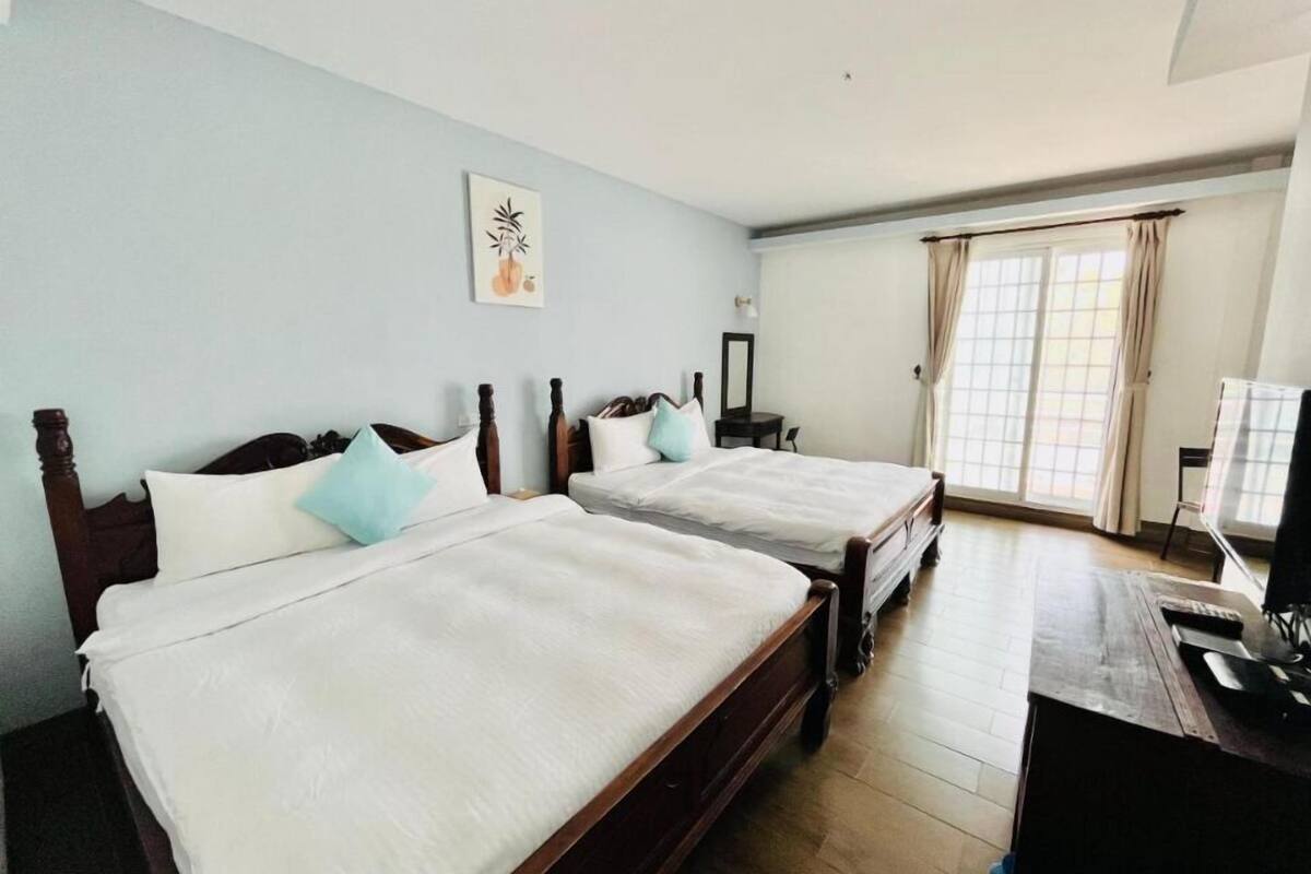 Habitación de hotel con dos camas de madera, un escritorio y una ventana con cortinas.