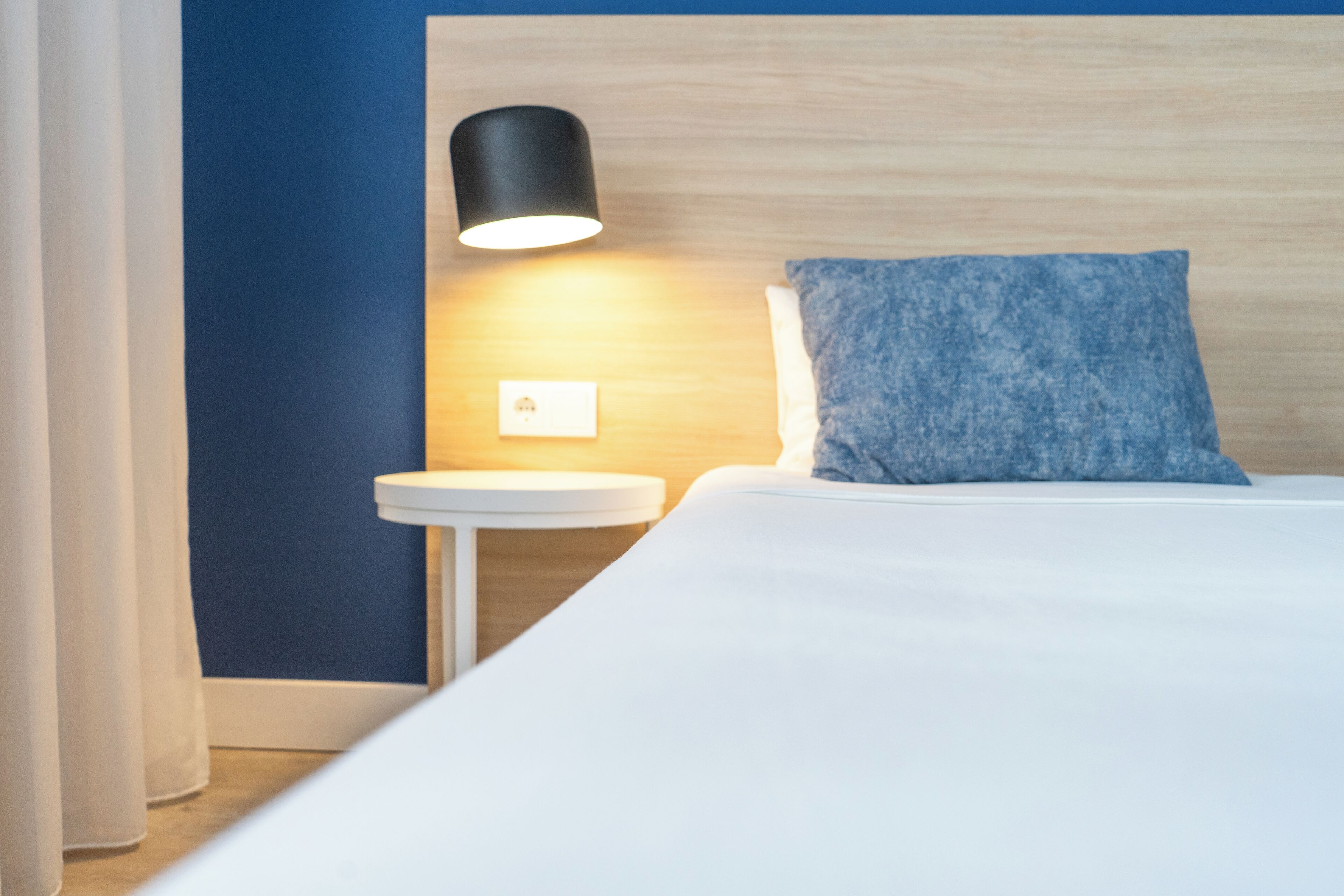 Et hotelværelse med en seng, et natbord, en lampe og en blå væg.