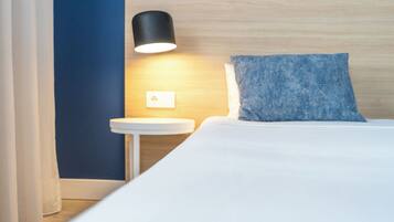 Et hotelværelse med en seng, et natbord, en lampe og en blå væg.