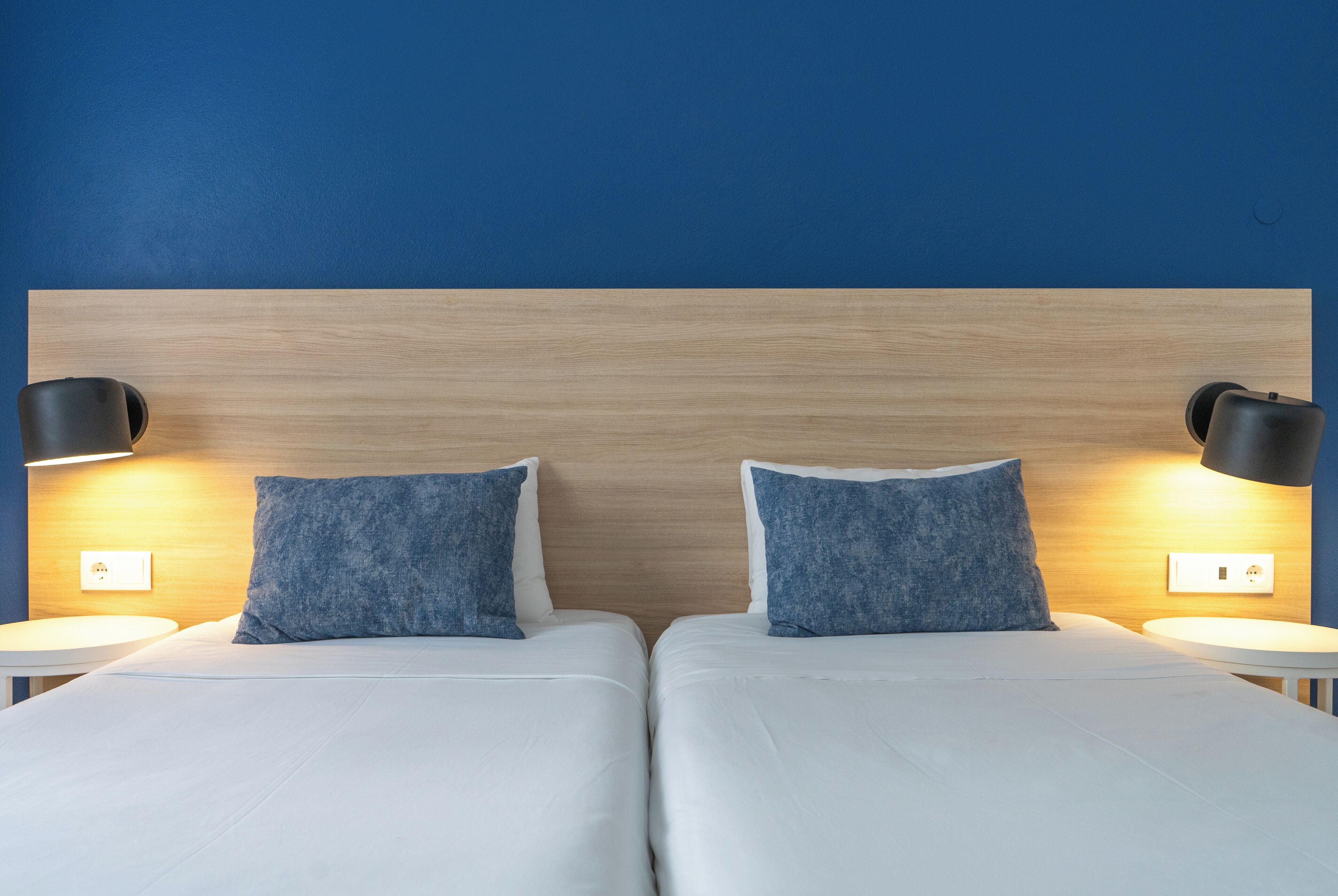 Habitación de hotel con dos camas, cabecero de madera y lámparas de noche.