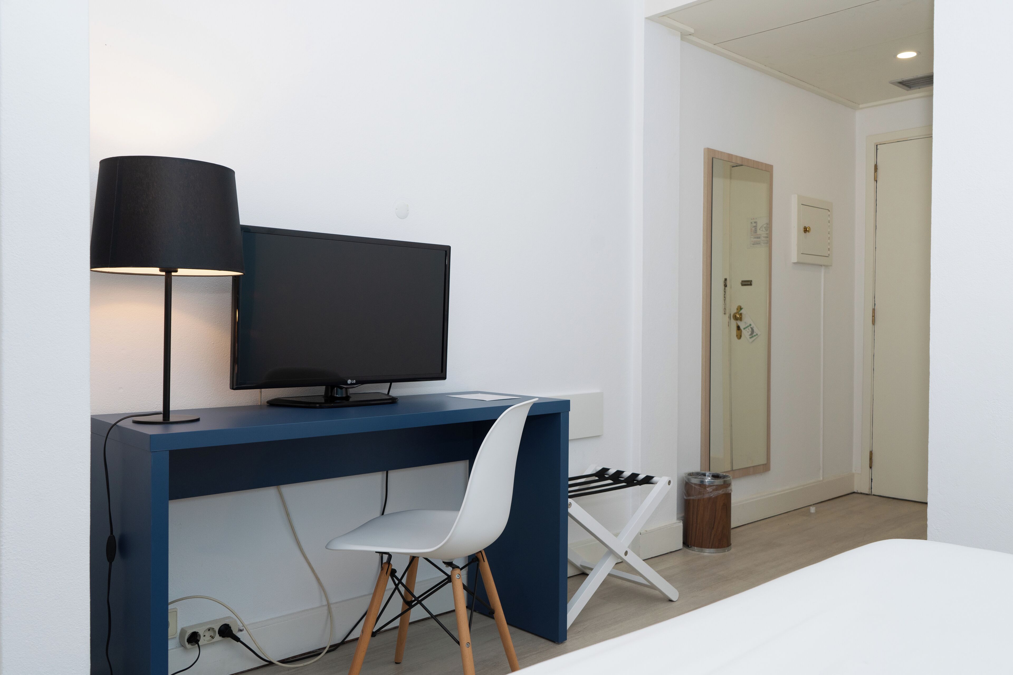 A modern room with a blue desk, a white chair, a flat-screen TV, and a lamp.