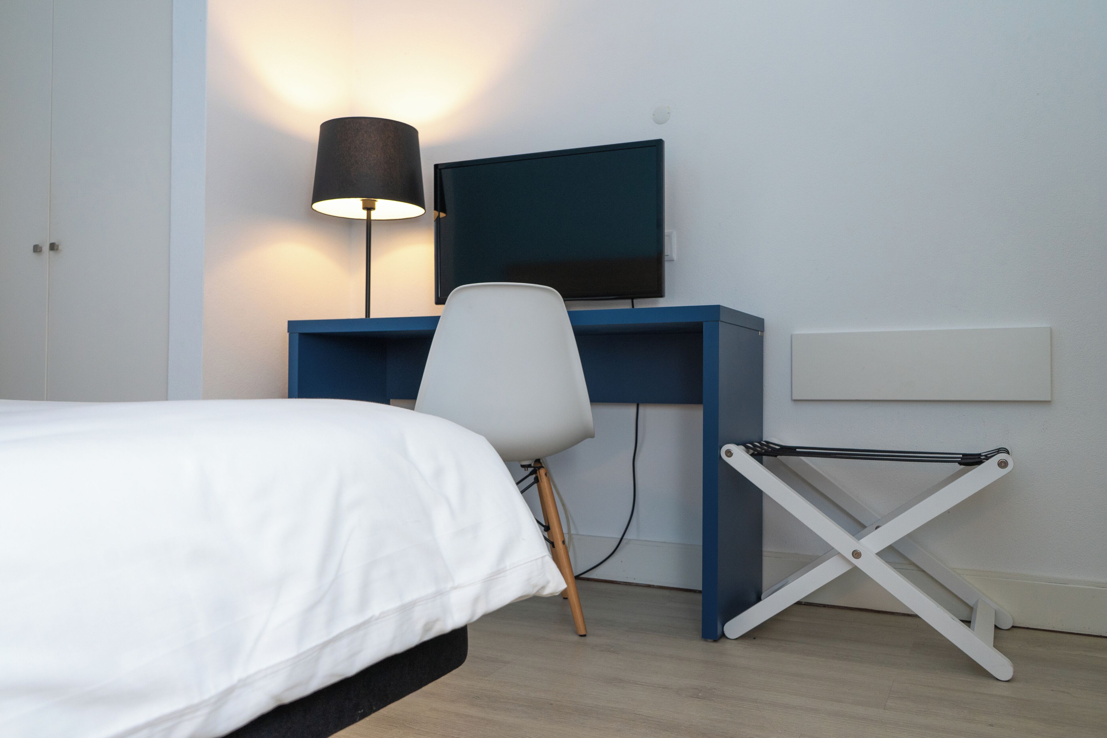 A bedroom with a bed, a desk with a chair, a TV, and a lamp.