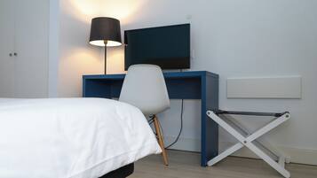 A bedroom with a bed, a desk with a chair, a TV, and a lamp.