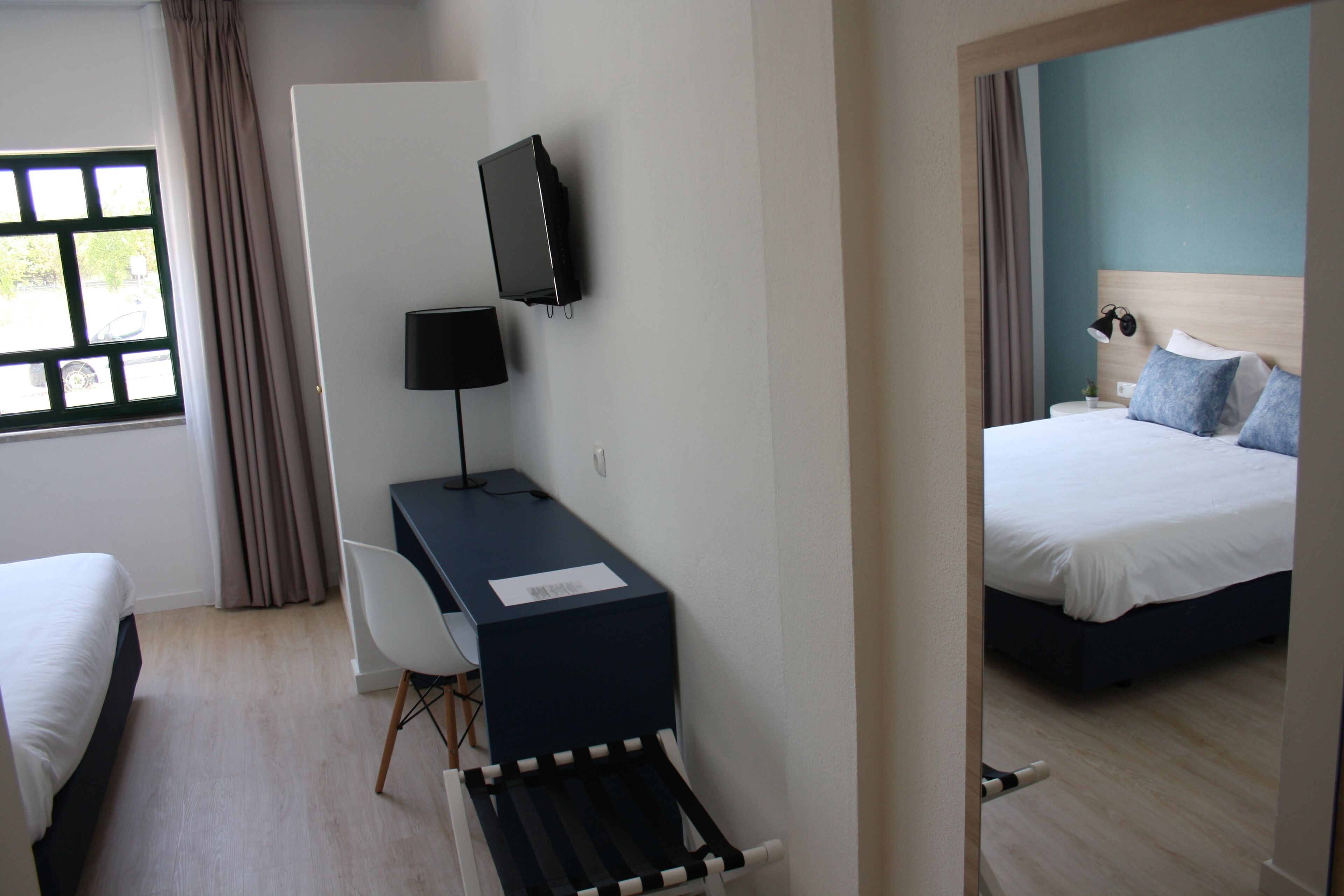 Habitación de hotel con cama, escritorio, silla, televisor y ventana con cortinas.