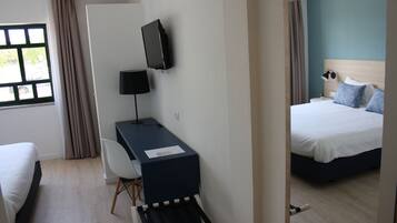 Habitación de hotel con cama, escritorio, silla, televisor y ventana con cortinas.