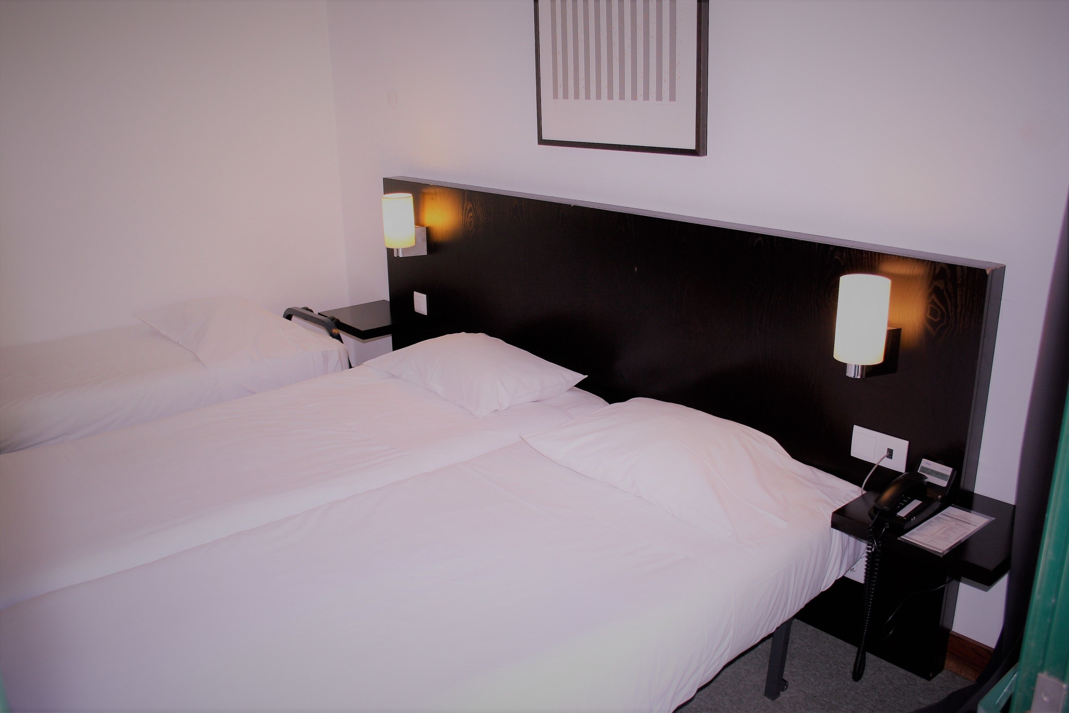 A double bed with white linens, a bedside table with a lamp, and a phone.
