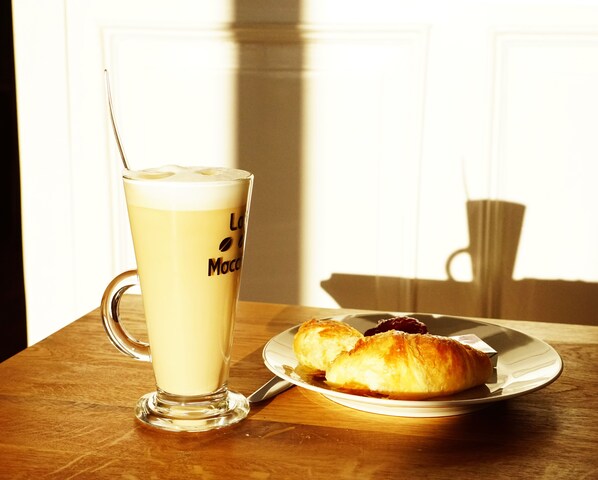 A glass of coffee with a straw on a wooden table next to a plate with croissants.