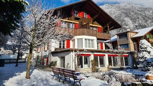 A multi-story wooden building with balconies, a bench, and a snow-covered landscape. - Adventure Guesthouse (Unterseen)