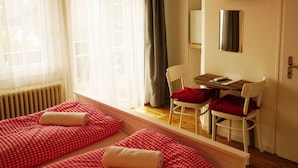 A room with a bed, a desk, a chair, a TV, and a radiator. - Adventure Guesthouse (Unterseen)