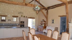 A rustic kitchen with exposed beams, a dining area with wooden chairs, and a stone wall. - Pretty dovecote in the countryside (monestier)