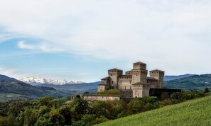 A historic castle with multiple towers, surrounded by lush greenery and mountains in the background. - La locanda del Borgo (Langhirano)