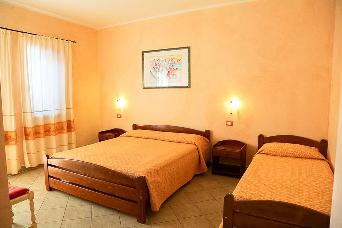 A hotel room with two wooden beds, a single chair, a nightstand, a wall-mounted light, and a framed picture.