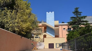 Un edificio con una escalera que conduce a un balcón, rodeado de árboles y una valla.
