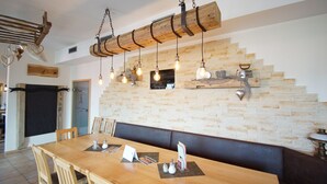 Una mesa de comedor de madera con sillas, un banco, lámparas colgantes y una pared de piedra.