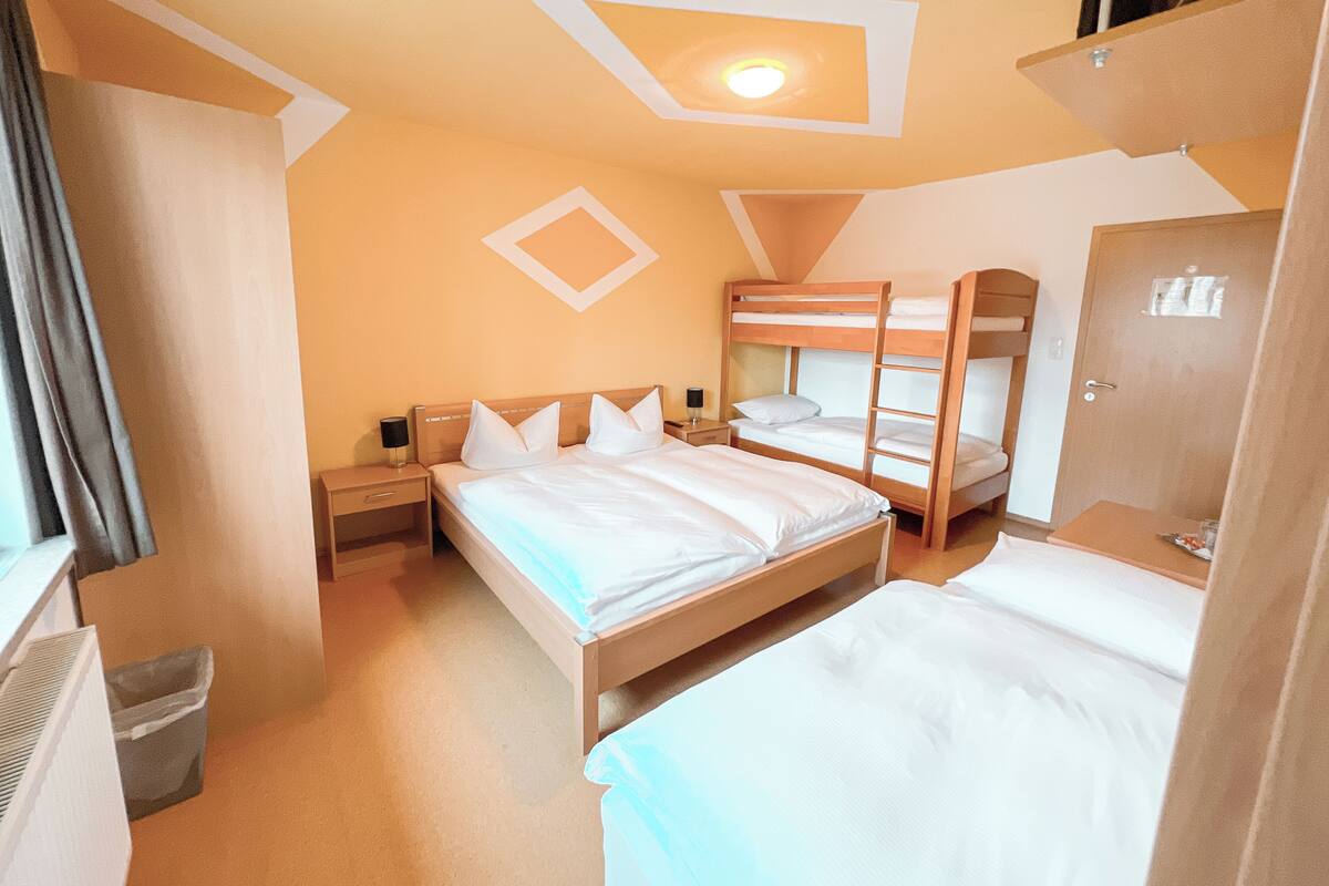 Una habitación de hotel con literas, una mesita de noche con lámpara y un pequeño cubo de basura.