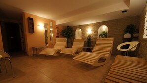 Un área de spa con tumbonas de madera, pared de piedra y suelo de baldosas.
