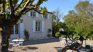 A white building with a gravel courtyard, white shutters, and a metal sculpture.