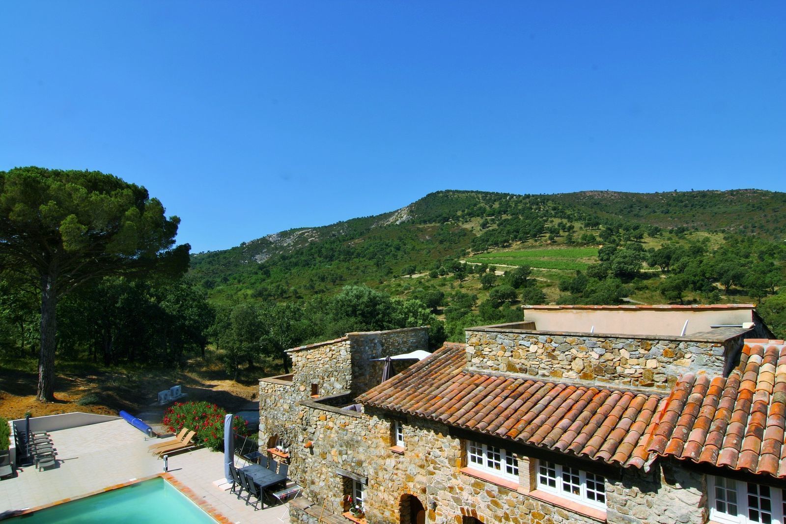 Un bâtiment en pierre avec un toit en tuiles, une piscine et une vue sur un paysage verdoyant, avec des arbres et des collines.