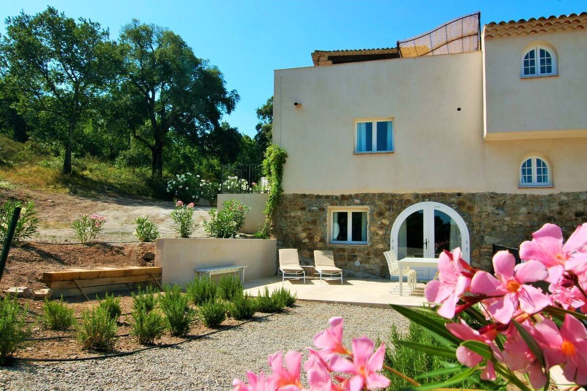 Un bâtiment à deux étages avec une façade en pierre, une porte blanche et un patio aménagé avec du mobilier d’extérieur.