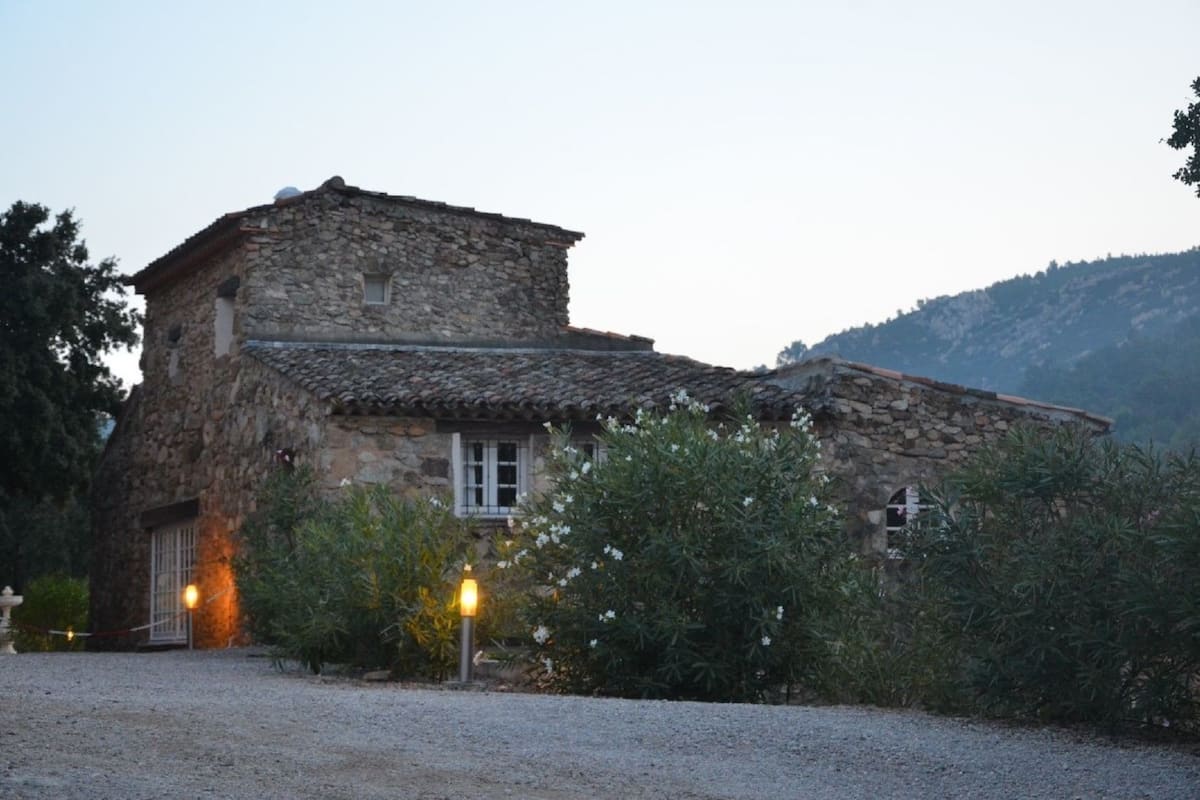 Un bâtiment en pierre avec un toit en tuiles, une porte en bois et une allée gravillonnée.