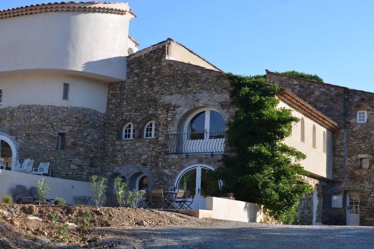 Un bâtiment en pierre doté d’une tour ronde, de fenêtres en arc de cercle et d’un espace extérieur aménagé pour s’asseoir.