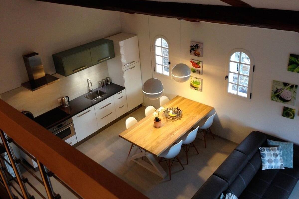 Une cuisine moderne avec des meubles blancs, une table à manger en bois et un canapé noir.
