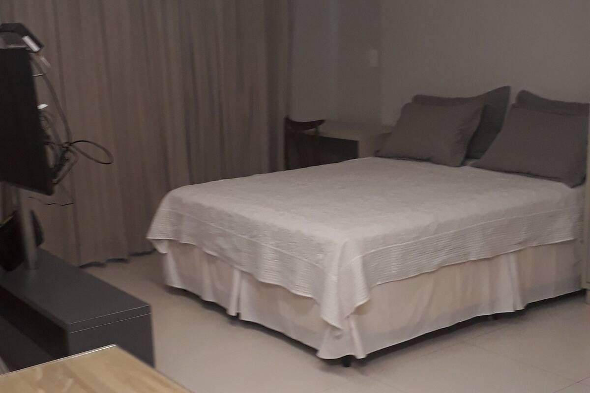 A hotel room with a bed, a desk, a TV, and a curtain.