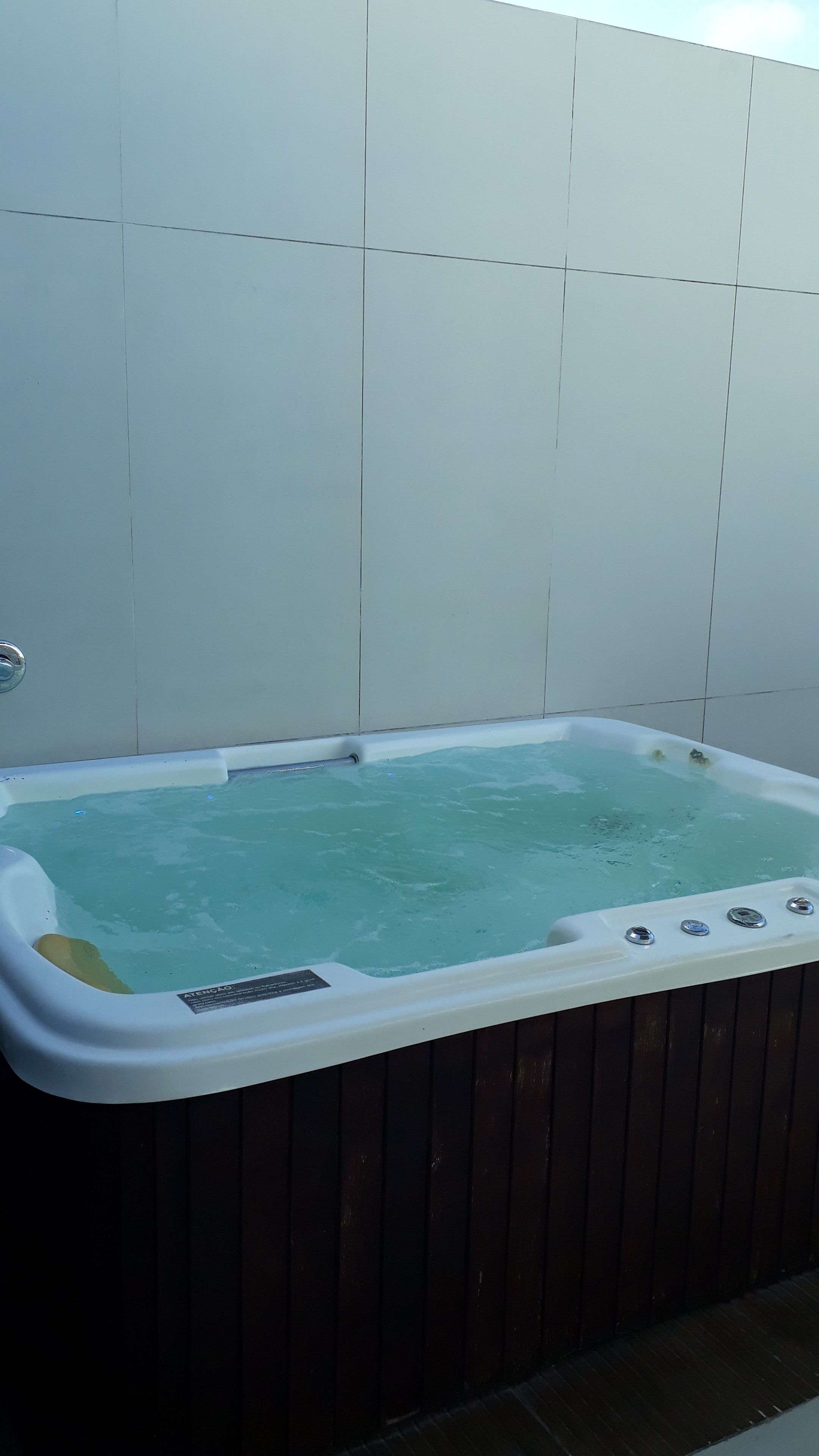 Ett bubbelbad med träpanel på utsidan, placerat framför en vägg klädd med kakel.