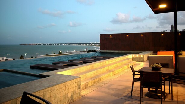 A rooftop pool area with a view of the sea and a distant pier. - Holanda's Prime - Praia de Tambaú (João Pessoa)