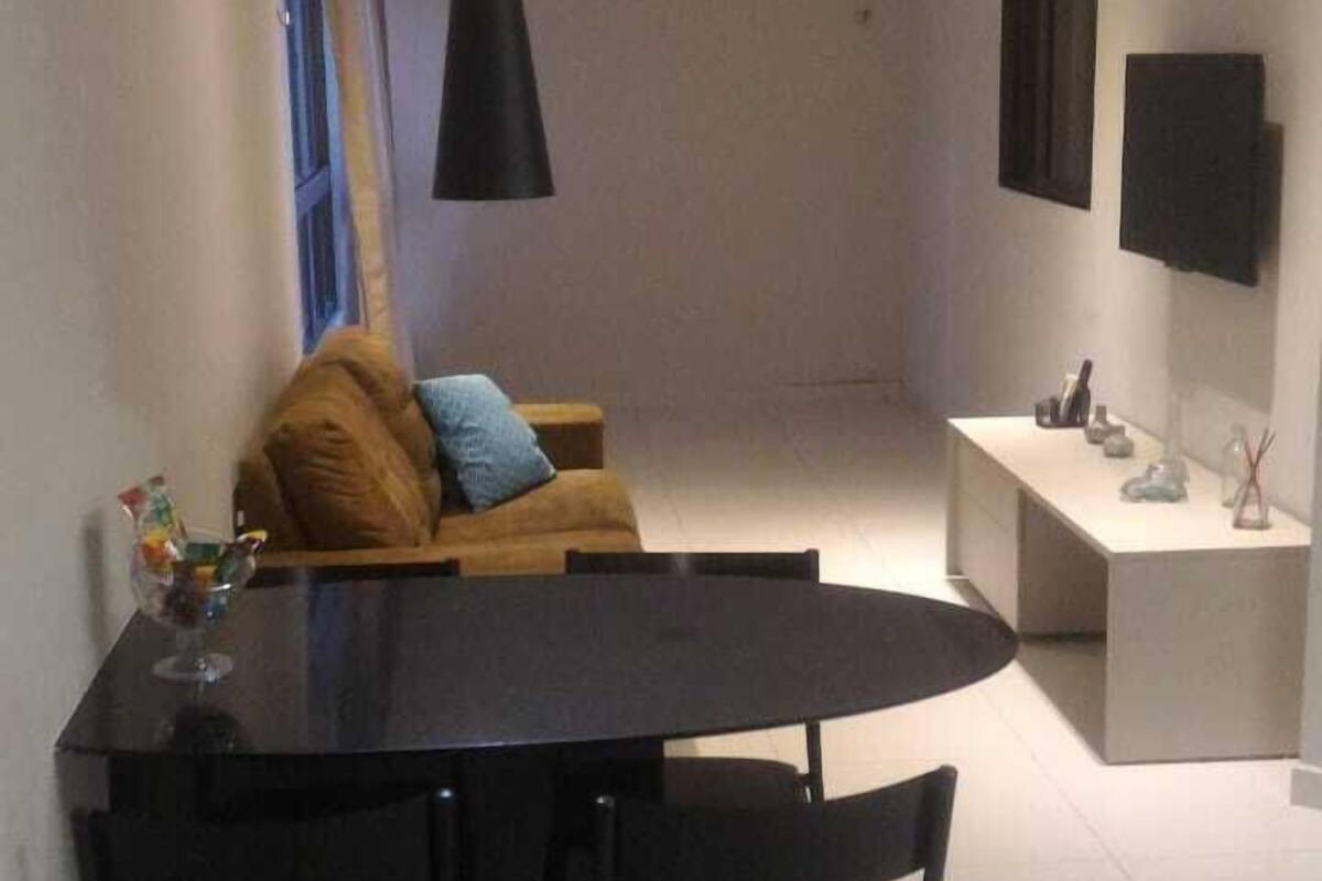 A modern dining area with a black table and chairs, a hanging pendant light, a sofa with cushions, and a white countertop with a sink and decorative items.