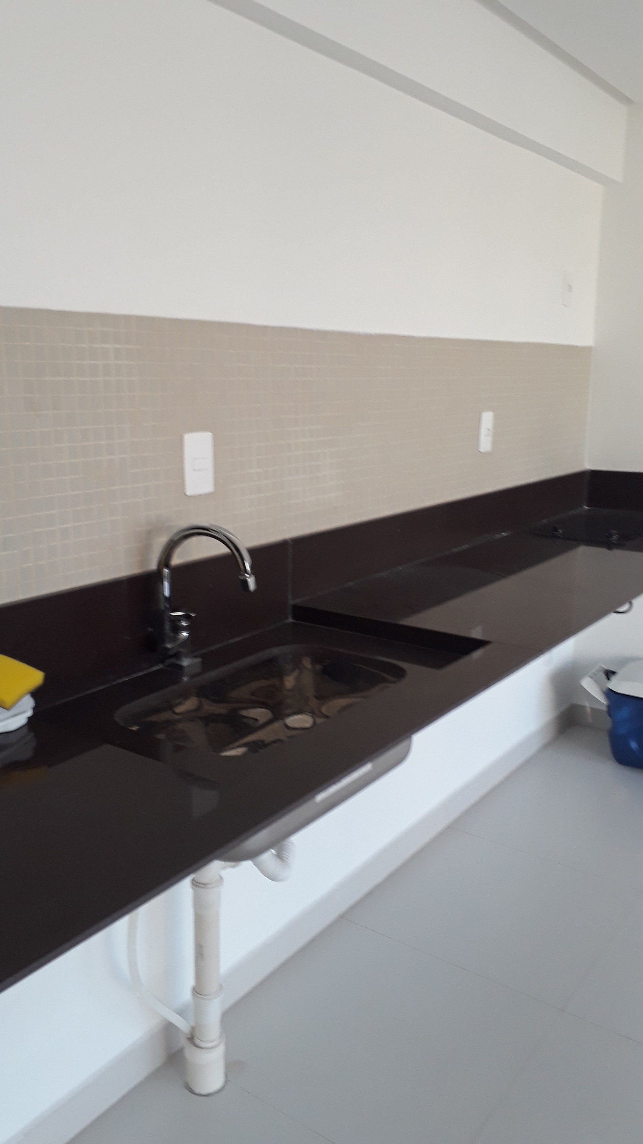 A kitchen with two sinks, a black countertop, and a tiled backsplash.