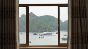 A view through a window with curtains, featuring a body of water with boats and a mountainous landscape in the background.