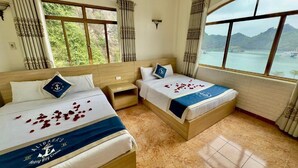 A hotel room with two beds, a large window, and a view of a body of water and mountains.