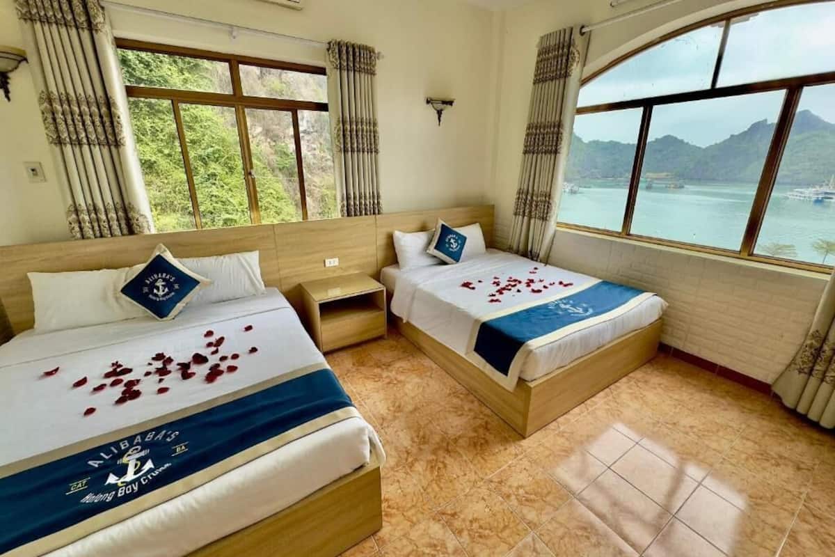A hotel room with two beds, a large window, and a view of a body of water and mountains.