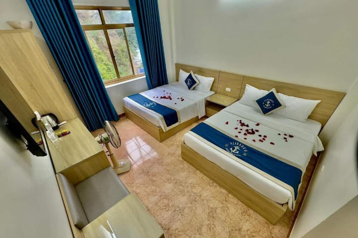 A hotel room with two beds, a wooden desk, and a window with curtains.