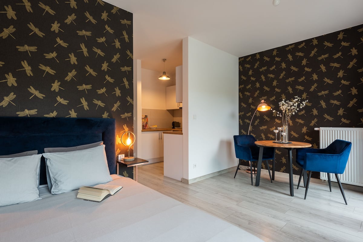 Une chambre d’hôtel moderne comprenant un lit, une petite table avec une lampe et un coin repas avec des chaises.
