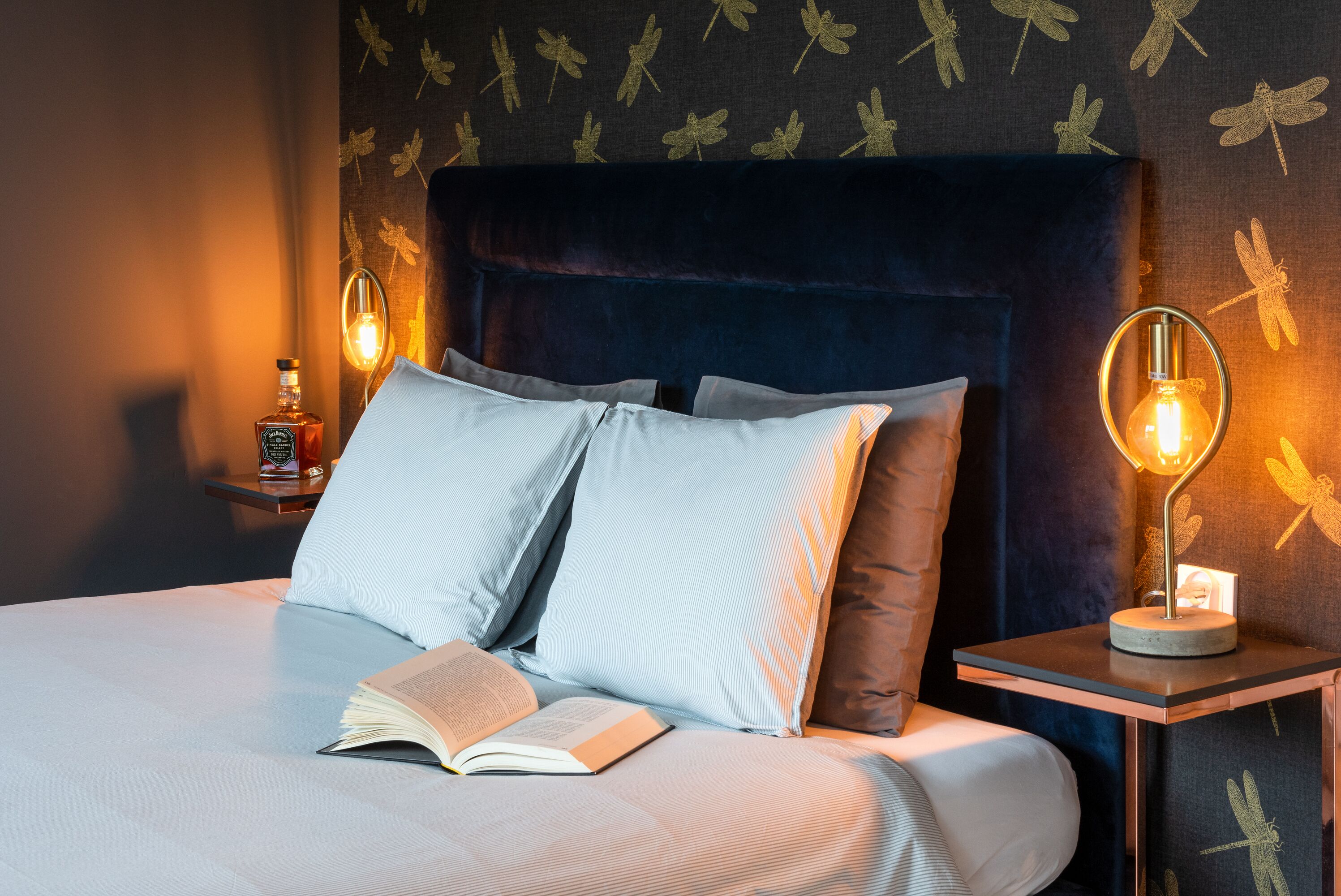 A neatly made bed with pillows, a book, and two bedside lamps.