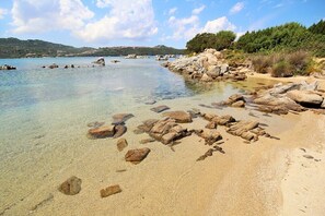 A beach with clear water, rocks, and greenery.