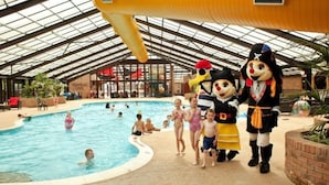 An indoor swimming pool with people swimming and playing, surrounded by a covered area with a glass roof. - Park Home in Marine Holiday Park (Rhyl)