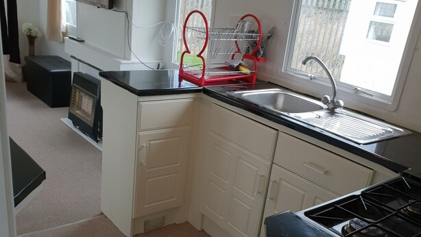 A compact kitchen with a stove, sink, and dish drying rack. - Park Home in Marine Holiday Park (Rhyl)