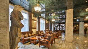 A spacious lobby with marble flooring, leather sofas, wooden tables, and a statue. - Hotel Wine Palace (Tbilisi)