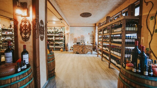A wine cellar with wooden barrels and shelves of wine bottles. - Hotel Wine Palace (Tbilisi)