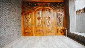 A room with a large wooden door with intricate carvings, a tiled wall, and a marble floor. - Hotel Wine Palace (Tbilisi)