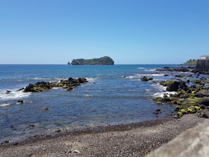 Paisaje costero con agua azul cristalina, costa rocosa y una pequeña isla al horizonte.