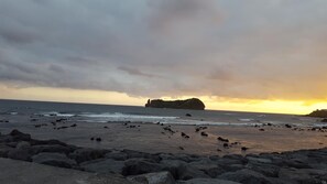 Une plage rocheuse, avec des vagues et une falaise à l’horizon, au moment du coucher du soleil.